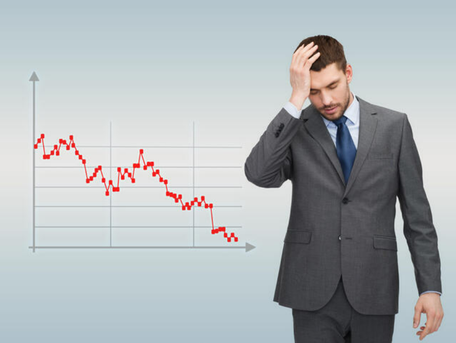 An image of a graph with a red line dropping towards the x-axis, with a man standing next to it holding his head in his hands